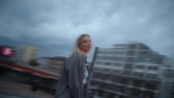 Lächelnde Frau mit urbanem Hintergrund blickt Kamera in Abendstadt. — Stockvideo