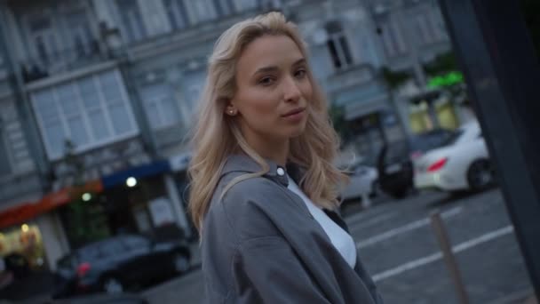 Блондинка жіноча модель, що йде у вечірньому місті біля дороги з автомобілями . — стокове відео
