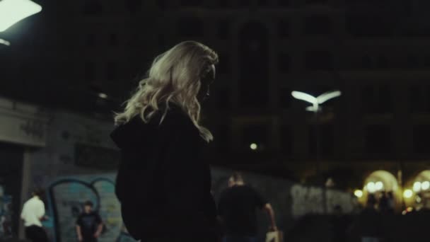 밤에 도시 건물에서 평상복을 입고 도시를 거닐고 있는 매력적 인 소녀. — 비디오