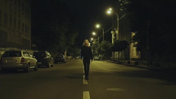 Kobieta spacerująca samotnie w nocy w luźnych ubraniach na drodze miejskiej. — Wideo stockowe