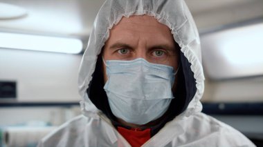 Sağlık görevlisi acil durum arabasındaki kameraya bakıyor. Koruyucu elbise giyen doktor.