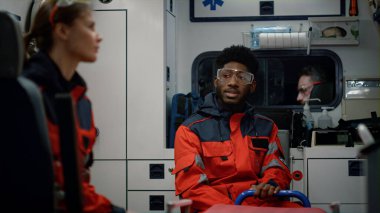 Paramedikler çağrı için acil durum aracına gidiyor. Doktor şoförle konuşuyor.