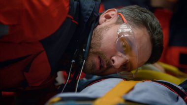 Paramedikler hastanın kalp atışlarını dinliyor. Kurban sedyelerde yatıyor.