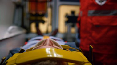 Ambulans arabasında sedyede yatan bir adam. Boyunluk takan erkek hasta.