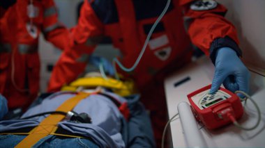 Ambulans görevlileri eldiven takıp ambulans arabasında hasta bakımı yapıyor.