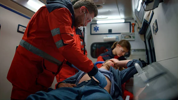 Karışık ırk sağlık ekibi acil durum arabasında adamın karnını inceliyor.