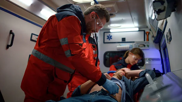 Paramédicos multiétnicos realizando primeros auxilios al hombre en vehículo de emergencia —  Fotos de Stock