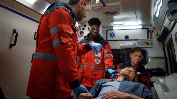 Multi paramédicos étnicos verificando pulso homem em macas em carro de emergência — Fotografia de Stock