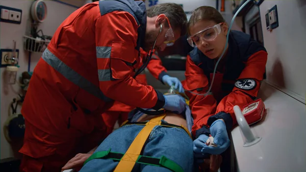 Mixed race doctors providing medical help of patient in ambulance car — Stock Photo, Image