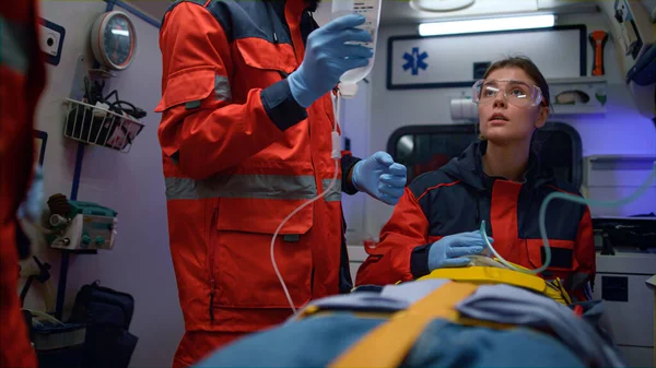 Ambulans arabasındaki sedyeli hastayla ilgilenen karışık yarış sağlık görevlileri.