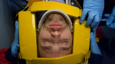 Sağlık görevlilerinin elleri hastayla ilgileniyor. Doktorlar adamın kafasını sedyede iyileştiriyor.