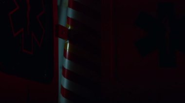 Karanlıkta mavi ve kırmızı acil durum ışıkları yanıp sönüyor. Ambulans arabası sokağa park edilmiş.