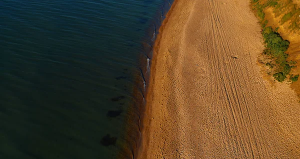 Temiz sıcak suyu olan havadan kumsal manzarası. Kumlu sahilde dalgalar sıçrıyor. 