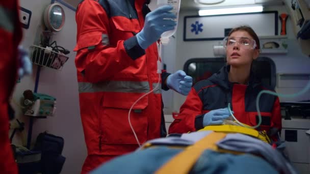 Vegyes fajú mentősök vigyáznak a betegre a mentőautóban. — Stock videók