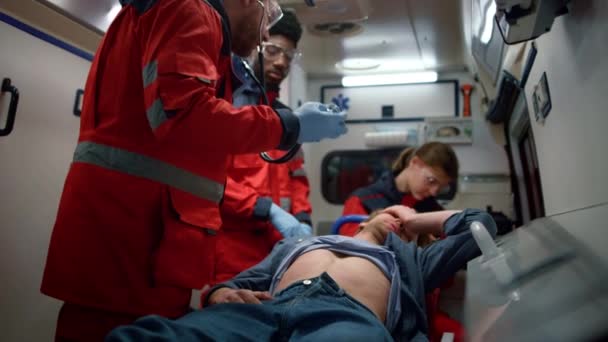 Equipo médico de carrera mixta examinando el abdomen del hombre en el coche de emergencia — Vídeos de Stock