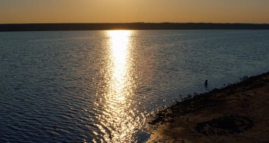 İnsansız hava aracı, altın gün batımında deniz kıyısında güneş yansıması yapar. Romantik güneş ışığı
