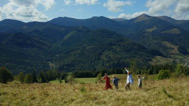Kids parents against mountains dancing grass enjoying time blue sky background