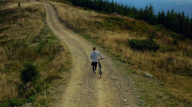 Man biking against mountains rocky road moving bike spring grass green trees.