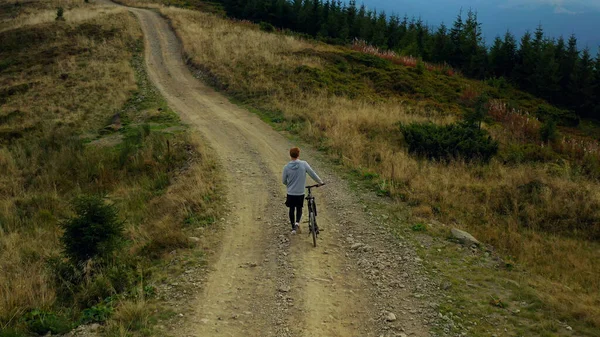 Man biking against mountains rocky road moving bike spring grass green trees.