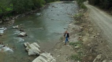 Hiker walking rocky river shore jumping on rocks among green trees spring day