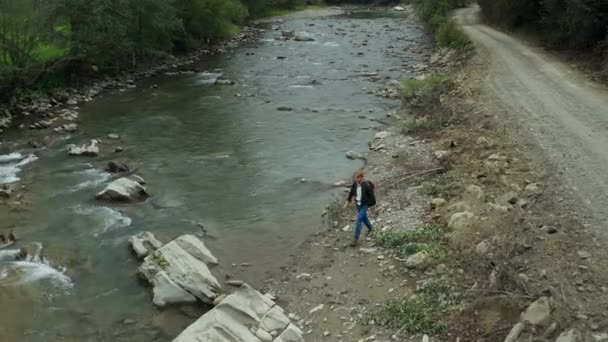 Hiker walking rocky river shore jumping on rocks among green trees spring day — Video Stock