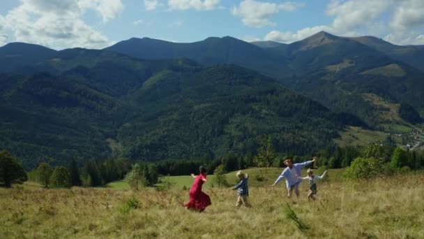 Kids parents against mountains dancing grass enjoying time blue sky background — Vídeo de Stock