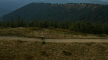Aerial mountain cycling man having fun hilly road against rocky green pikes