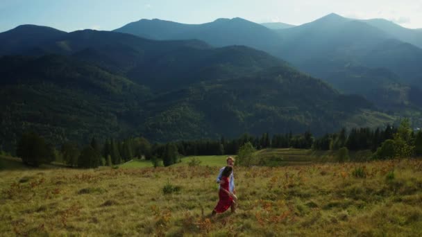 คนรักในภูเขาเดินหญ้าเพลิดเพลินกับภูมิทัศน์ที่น่าตื่นตาตื่นใจ พื้นหลังฟ้าสีฟ้า — วีดีโอสต็อก