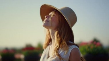 Pretty girl taking off sunhat in summer day. Cheerful woman enjoying sunlight.