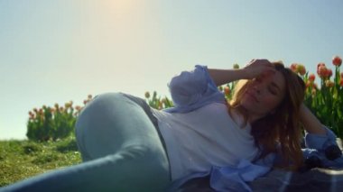 Relaxed woman lying in tulip garden. Smiling lady playing hair in soft sunshine.