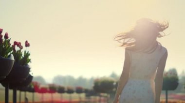 Smiling woman walking in garden. Emotional girl touching hair in sun reflection.