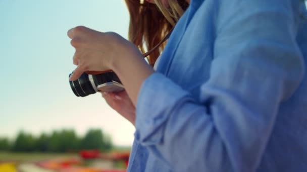 Крупним планом жінка тримає професійну фотокамеру в квітучому саду на відкритому повітрі — стокове відео