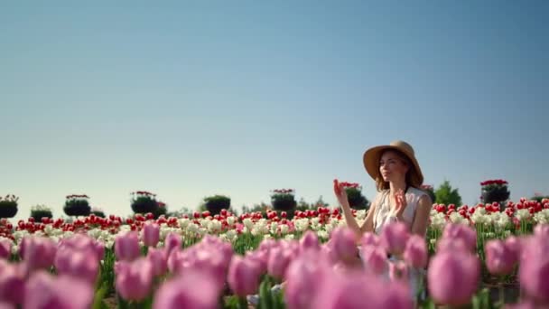 Young gentle woman in hat enjoying sunlight in blooming floral landscape. — Vídeo de stock