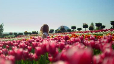 Playful woman flirting in spring flower garden. View of tulip park landscape.