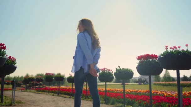 Back view of relaxed girl with camera walking in summer flower park in sunshine. — Vídeo de stock