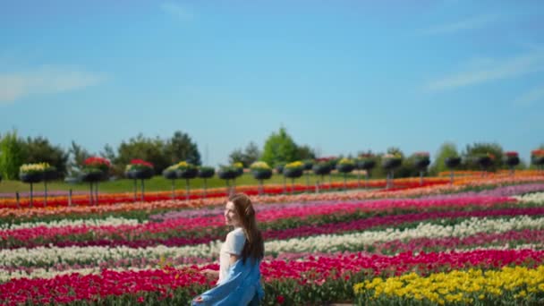 Ευτυχισμένο κορίτσι τρέχει σε φόντο λουλουδιών σε εξωτερικούς χώρους. Νεαρή γυναίκα στο λιβάδι της τουλίπας. — Αρχείο Βίντεο
