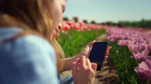 Achteraanzicht van jonge vrouw aanraken smartphone scherm met vingers in bloemenveld — Stockvideo