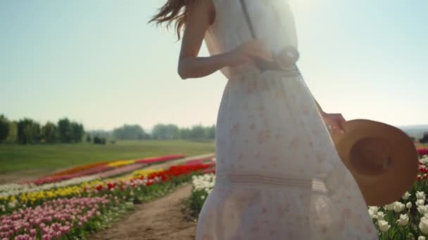 Young woman with camera and straw hat turning around in beautiful tulips garden. — Vídeo de stock