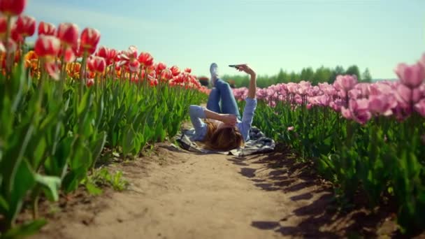 Квітучий тюльпан поданий навесні дівчина дивиться на екран мобільного телефону в сонячний день — стокове відео