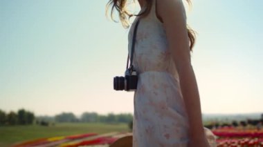 Unrecognizable woman with camera looking back at garden with spring flowers. 