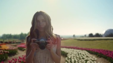 Portrait beautiful lady with camera. Happy woman walking in garden of flowers.
