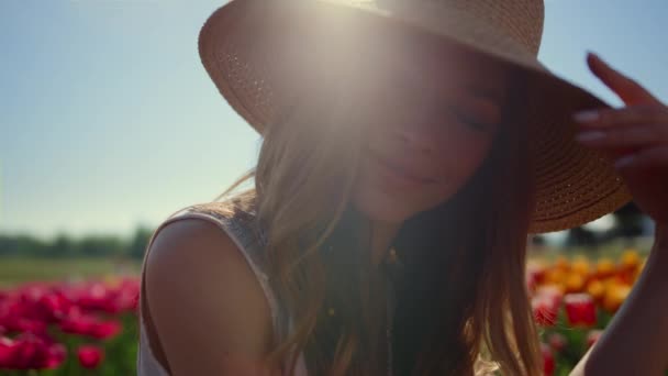 Beautiful woman portrait taking off straw hat in sunlight in floral background. — Stock video