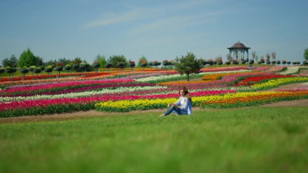 Kwitnący park wiosenny i młoda kobieta relaksująca się na świeżej zielonej trawie. — Wideo stockowe