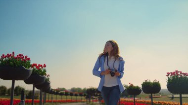 Happy female photographer running in slow motion in blooming park in sunny day.