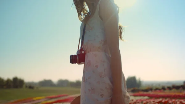 Nierozpoznawalna kobieta z kamerą patrząca wstecz na ogród z wiosennymi kwiatami. — Zdjęcie stockowe