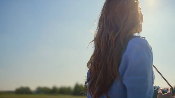 Back view of unknown woman with photo camera enjoying sunlight in spring garden. — Stockfoto