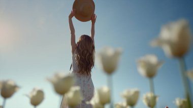 Unknown woman silhouette with sunhat stretching hands to blue sky in sunny day.