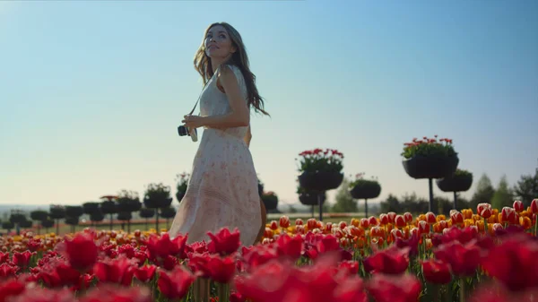 Beautiful girl with camera walking through tulip field. Woman smiling in garden. — Foto Stock