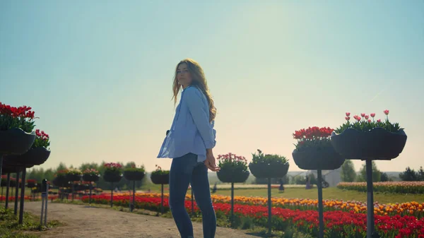 Back view of relaxed girl with camera walking in summer flower park in sunshine. — 图库照片