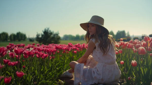 Macchina fotografica che si muove lungo la strada in campo tulipani rossi con ragazza in cappello seduta in fiori — Foto Stock